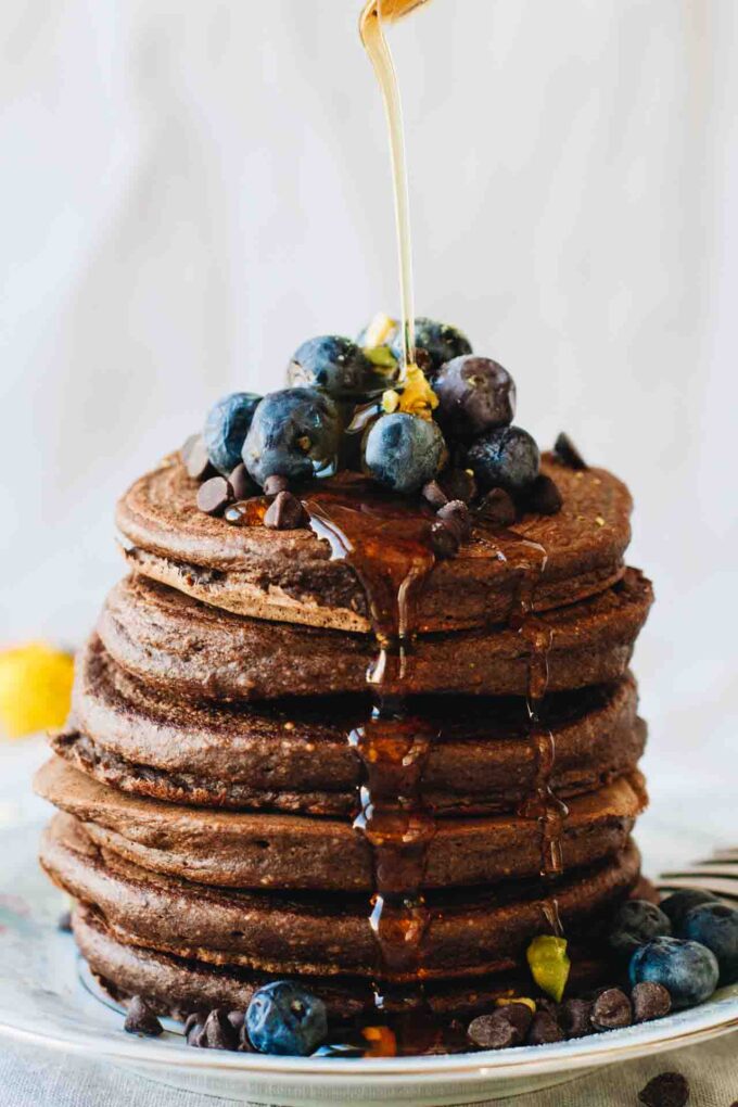 Chocolate Protein Pancakes with blueberries and syrup pouring over them! Loaded with superfoods, protein, fruit, eggs, and rolled oats. They also happen to be gluten and dairy free!