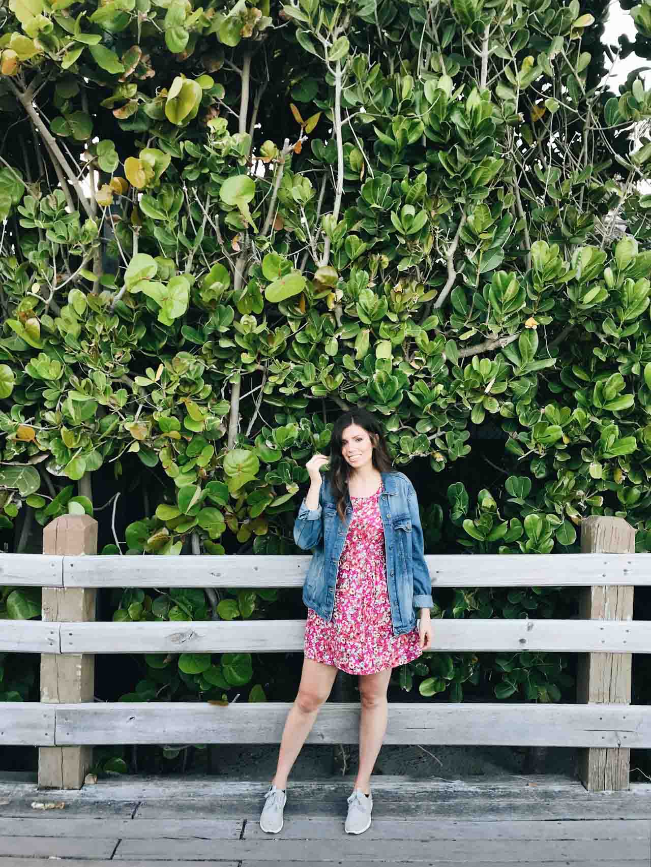 Christine from Jar Of Lemons on Our Trip To Miami standing in front of greenery outside by a fence