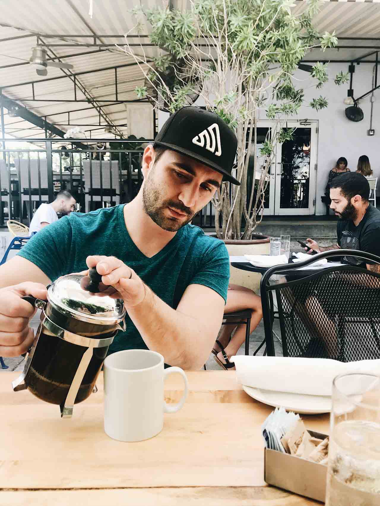 Man pouring french pressed coffee at an outdoor coffee shop.