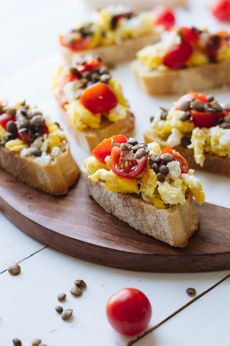 Tomato & Lentil Breakfast Bruschetta with eggs on a baguette on a wooden surface. 