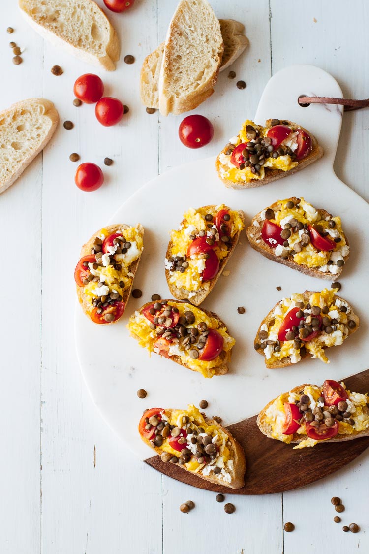 Overhead shot of Tomato & Lentil Breakfast Bruschetta on a cutting board and wooden table