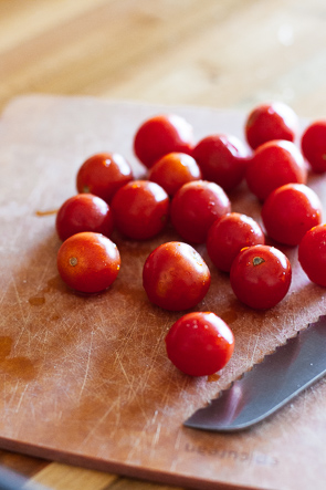 Grape tomatoes on a cutting board next to a knife.
