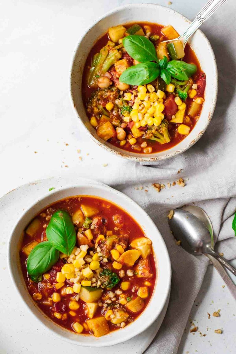 Easy Vegetarian Summer Chili in two bowls on a white marble table with a napkin and spoons. By Jar Of Lemons