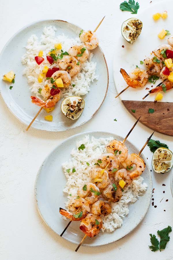 Spicy Grilled Shrimp w/ Pineapple Sauce served with rice, cilantro, and fresh lime juice on two white plates.