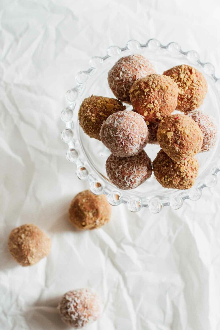 Strawberry Cheesecake No-Bake Energy Bites on white wax paper and a cake stand.