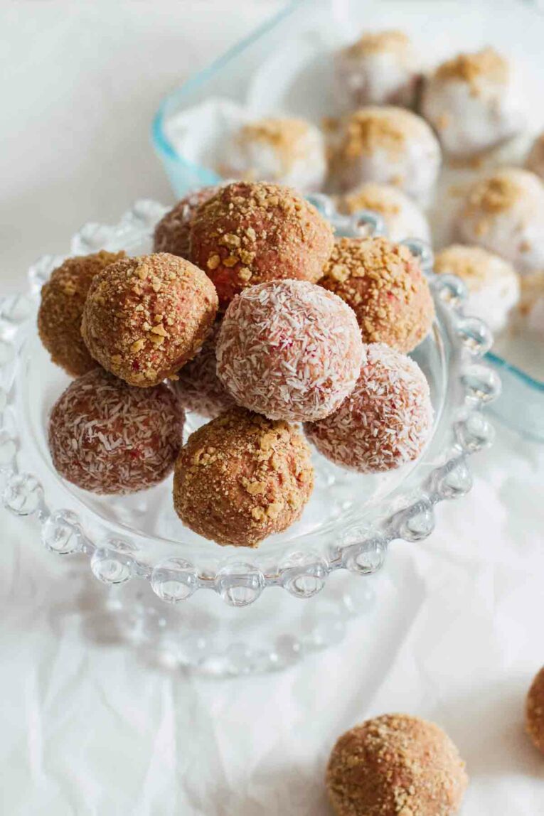 Strawberry Cheesecake No-Bake Energy Bites made with rolled oats, creamy cashew butter, vegan protein powder, coconut oil, agave, and freeze dried strawberries served on a cake stand.