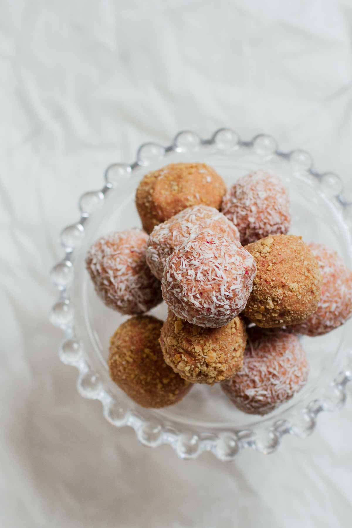 Overhead shot of Strawberry Cheesecake No-Bake Energy Bites made with rolled oats, creamy cashew butter, vegan protein powder, coconut oil, agave, and freeze dried strawberries on a cake stand.