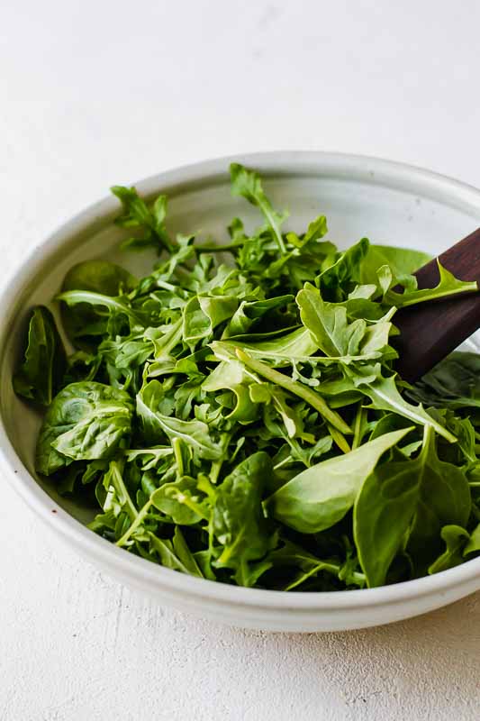 Arugula and spinach in a white bowl on a white table