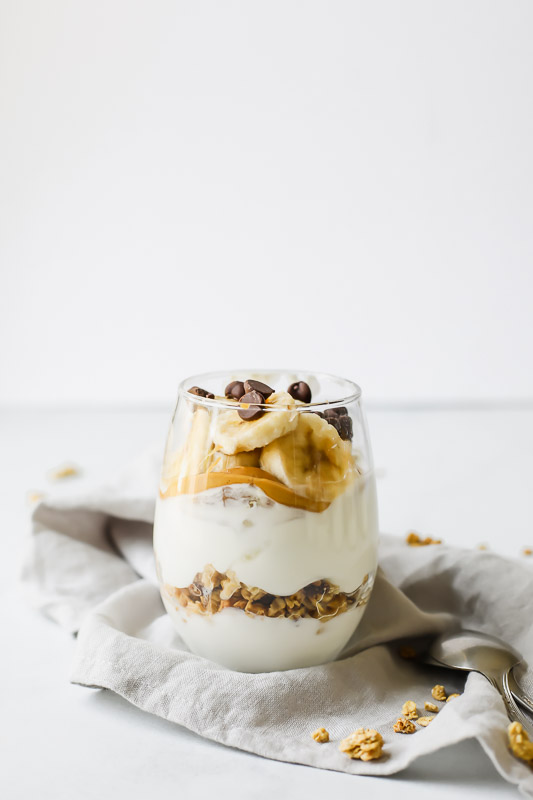 Banana Peanut Butter Chocolate Protein-Loaded Yogurt Parfait in a glass on a grey cloth.