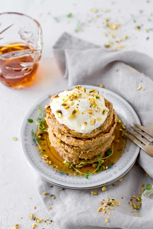 Stack of Simple 3-Ingredient Protein Pancakes served on a floral plate next to syrup.