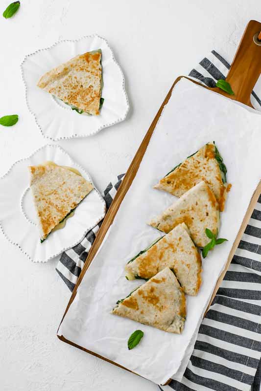 Overhead shot of 5-Minute Spinach Vegetarian Quesadillas lined on a cutting board and served on two white plates.