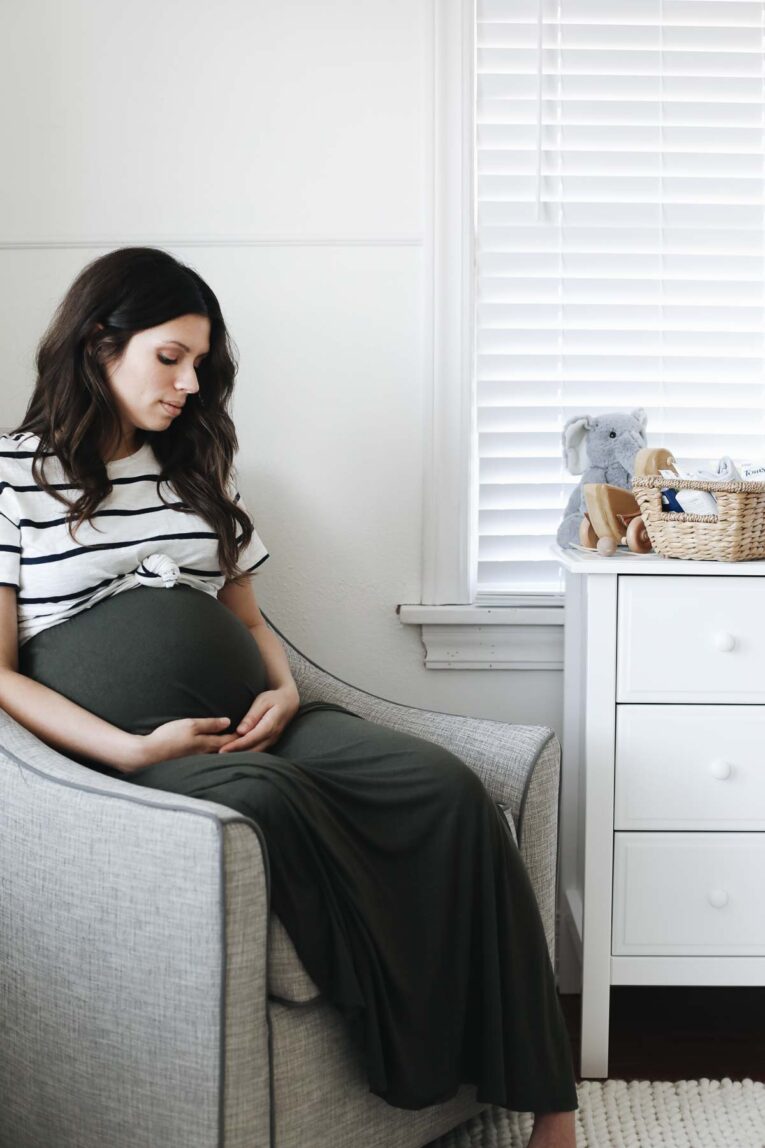 expecting mother sitting in chair in nursery.