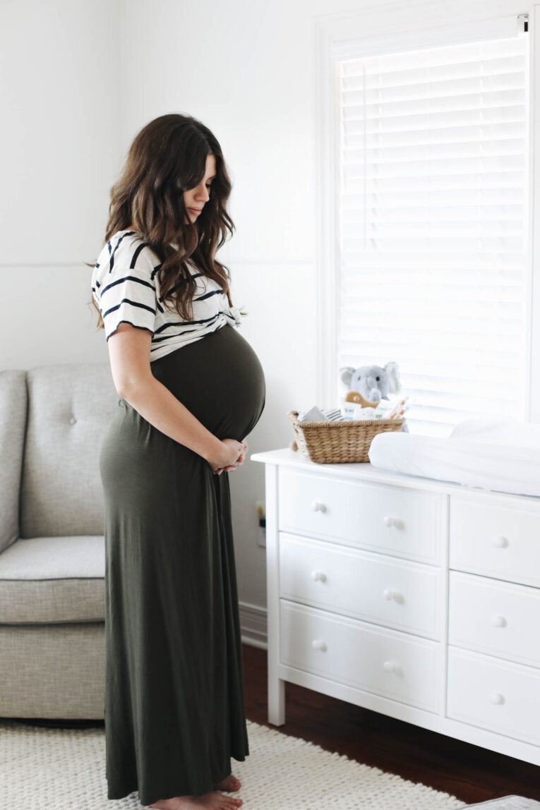 Woman standing in nursery holding her baby bump.