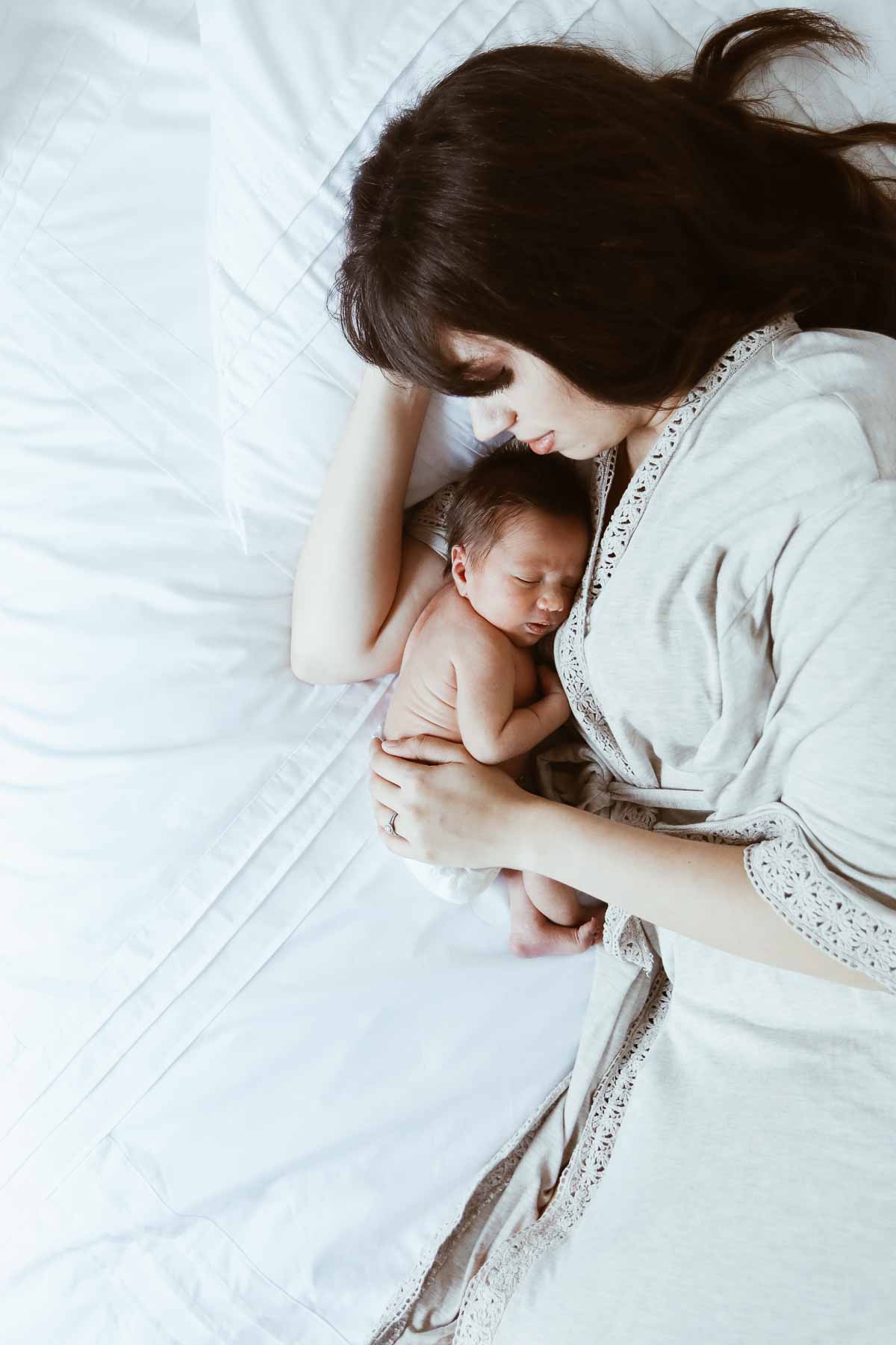 mom laying next to newborn baby in bed.