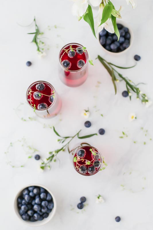 Overhead shot of  Blueberry Thyme Mimosas served in 3 glasses next to small bowl of blueberries.
