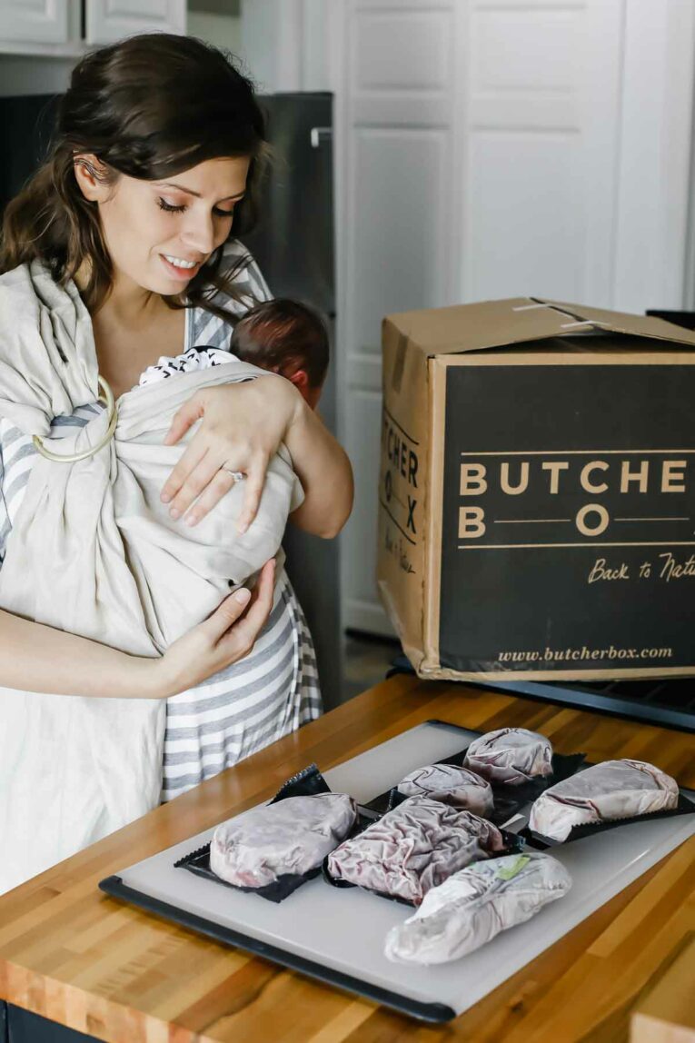 New mom holding baby next to butcher box.