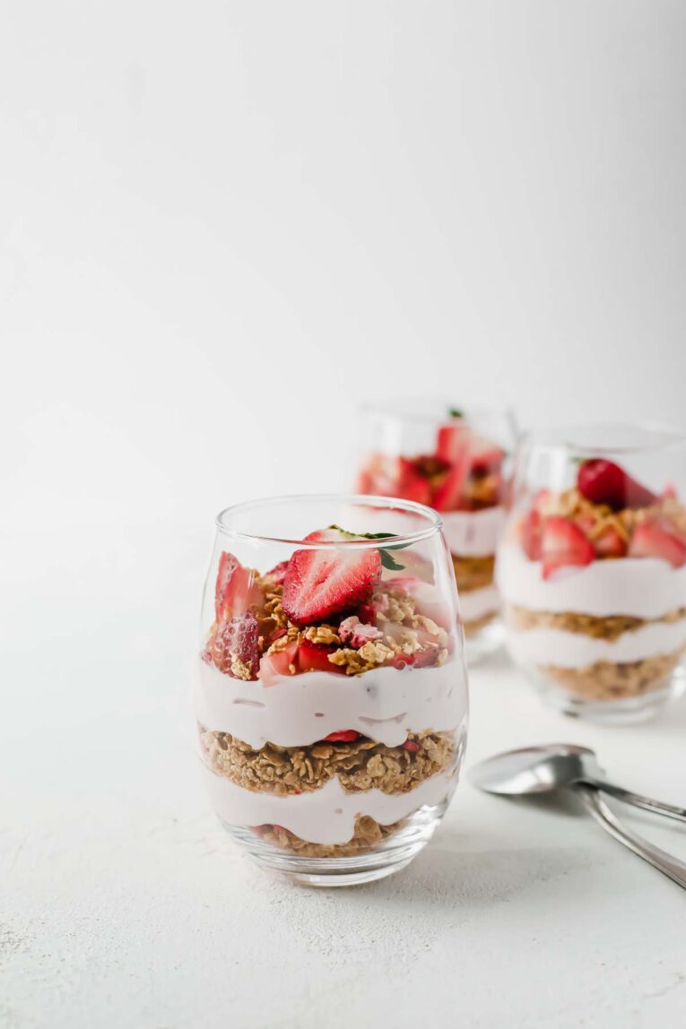 Side view of 5-Minute Strawberry Cheesecake Breakfast Parfait in glass jars newt to two spoons.