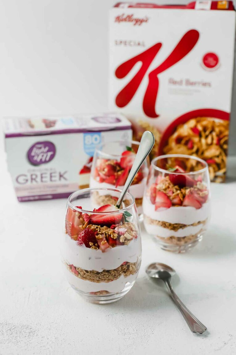 5-Minute Strawberry Cheesecake Breakfast Parfait in glass jars with yogurt and cereal in background.