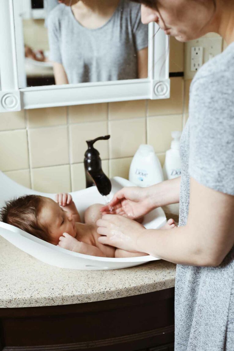 Mom giving newborn baby a bath in the bathroom sink.