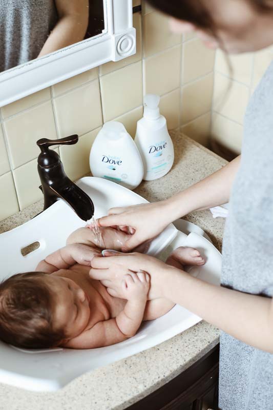 Mom giving baby a bath in the bathroom sink with Dove products.