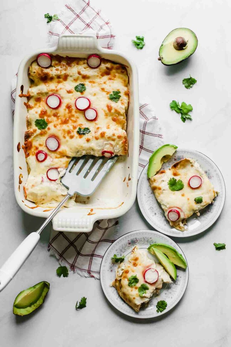 Overhead shot of Skinny Creamy Chicken Enchiladas in a white baking dish being served onto small plates.