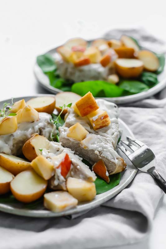 Slow Cooker Pork Chops And Potatoes W/ Apples served on a white plate with a fork.