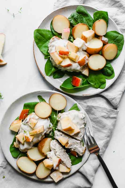 Slow Cooker Pork Chops And Potatoes W/ Apples served on two white plates.