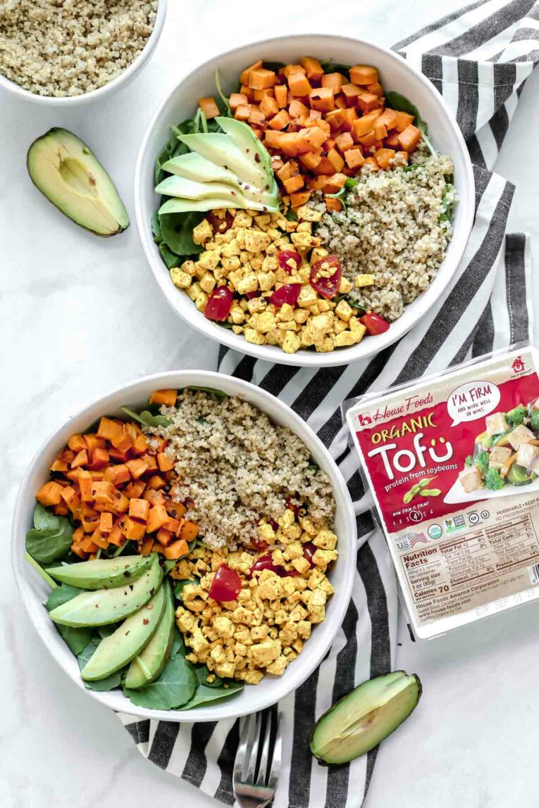 Overhead shot of 2 Tofu Scramble Vegan Breakfast Bowls served in white bowls next to package of Tofu. 