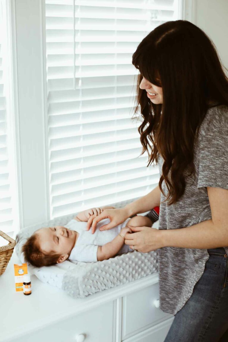 mom making baby smile while he's laying on a changing table next to a window.