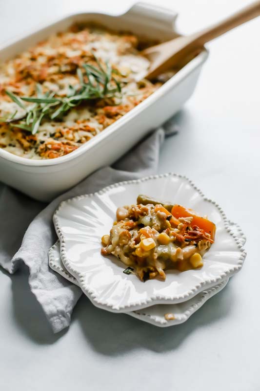 white plate with baked mixed vegetables next to baking dish with vegetables.