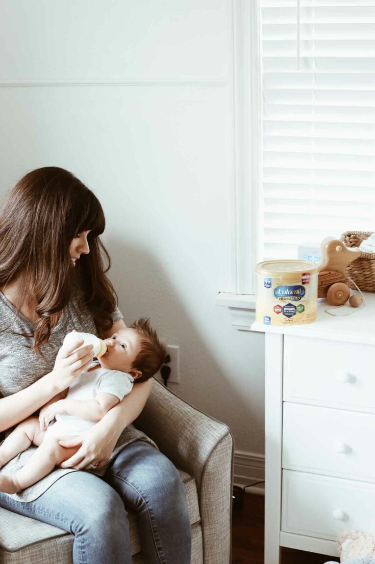 mom sitting in nursery giving her baby a bottle.