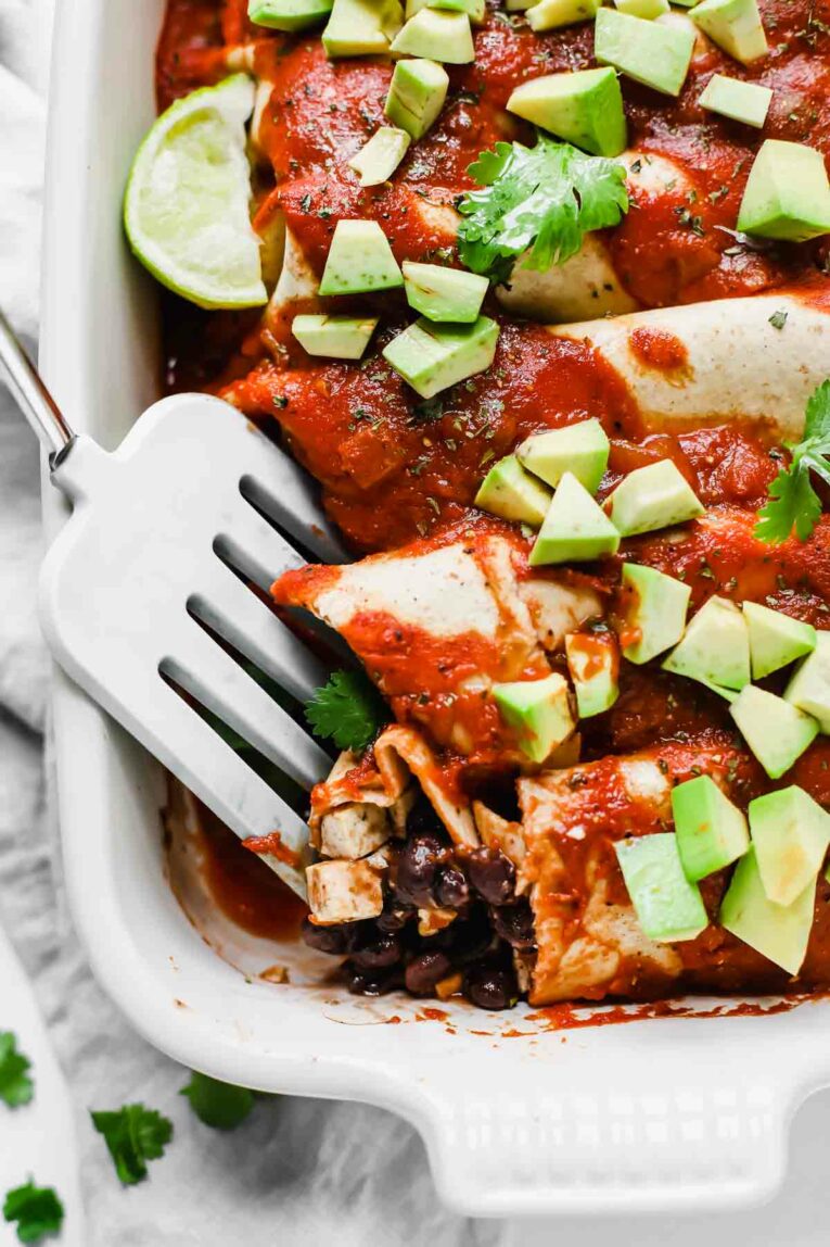 Spatula scooping into 5-Ingredient Vegan Enchiladas in a white dish.
