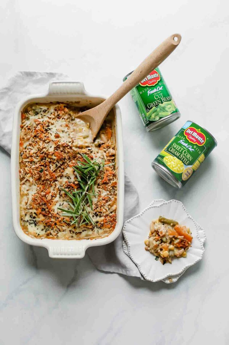 Baked Mixed Vegetable Casserole in a white baking dish next to cans of vegetables.