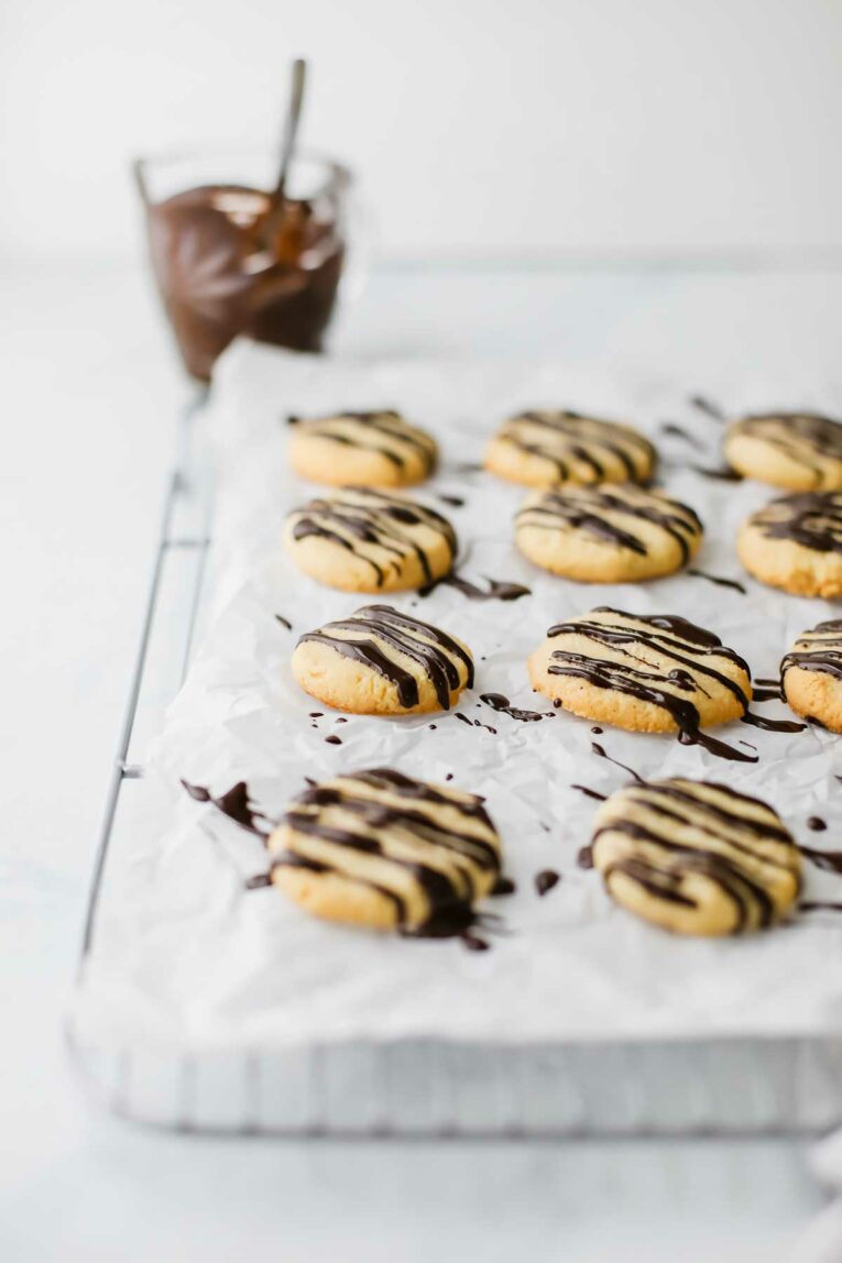 Side angle of Favorite Gluten-Free Almond Cookies on a cooling rack with Dark Chocolate drizzled over top.