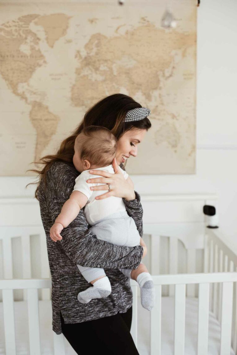 Mom holding baby next to crib.
