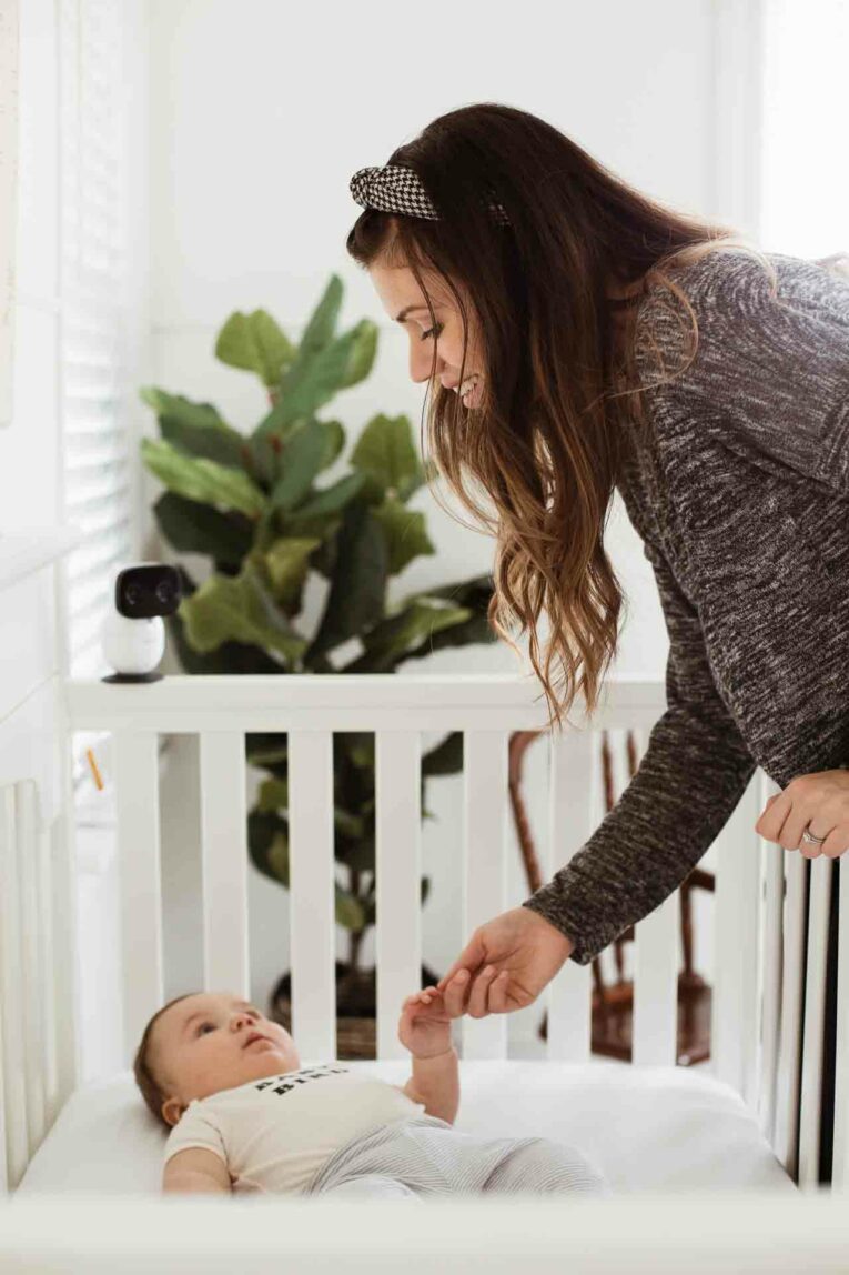 mom leaning over crib to hold baby's hand.