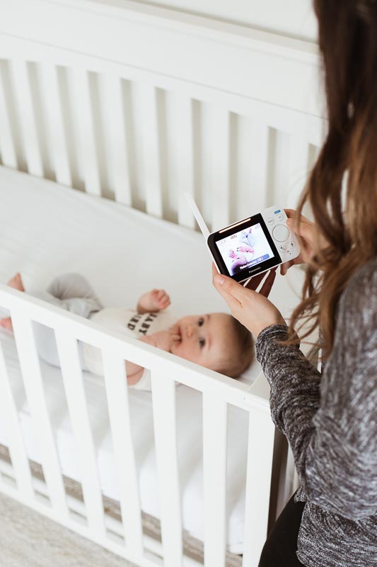 Mom holding Panasonic monitor next to crib with baby.