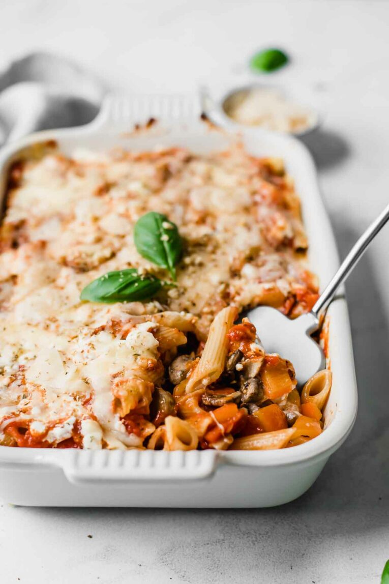 This Easy Vegetarian Baked Ziti Recipe can be made in 30 minutes and is perfect for a quick, healthy weeknight dinner! Made with mushrooms, zucchini, bell pepper, cottage cheese, and delicious ziti pasta. Healthy comfort food at it's finest! Vegetarian Baked Ziti in a casserole dish over a marble table top. Topped with fresh basil and walnuts.