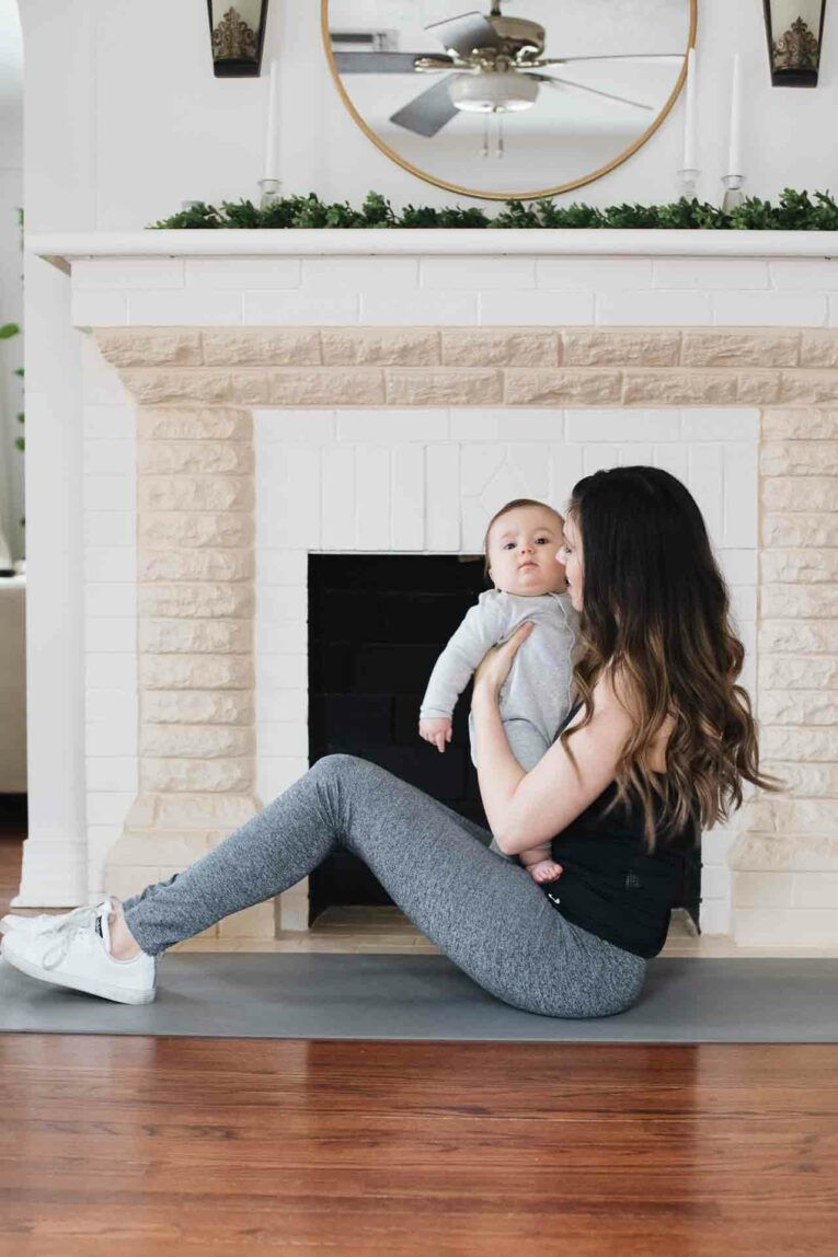 Woman in fitness clothes sitting on yoga mat holding baby