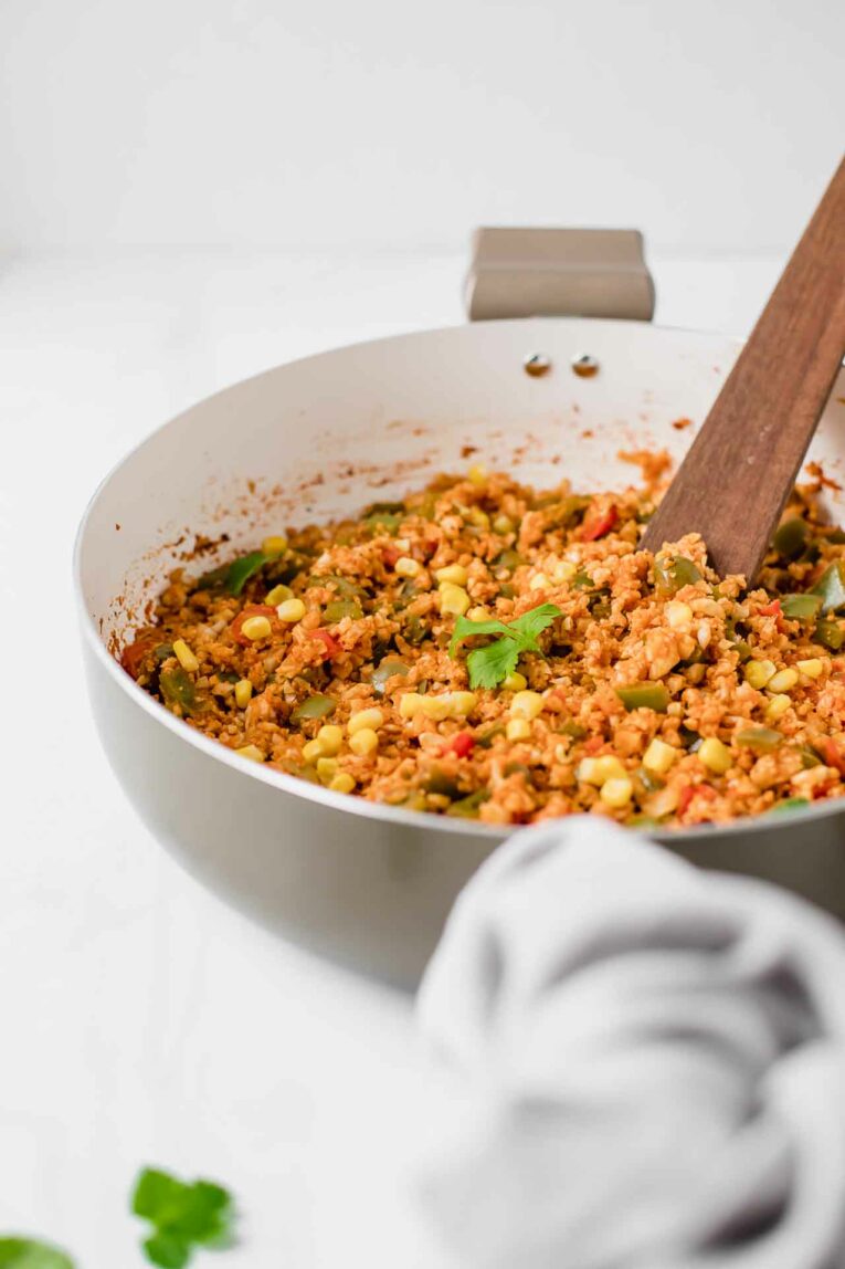 Savory, simple, and healthy. This 30-Minute Mexican Cauliflower Rice recipe is the best ever and is vegan, vegetarian, gluten-free, dairy-free, and paleo. It's perfect for dinner tonight! 30-Minute Mexican Cauliflower Rice in a pan on a white table served with cilantro.