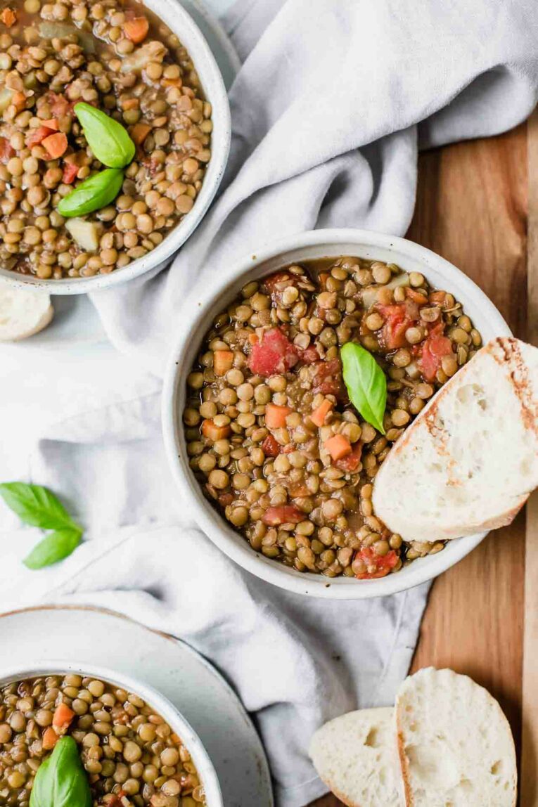 Close up of a bowl of vegan lentil soup topped with fresh basil and served with toasted baguette slices.