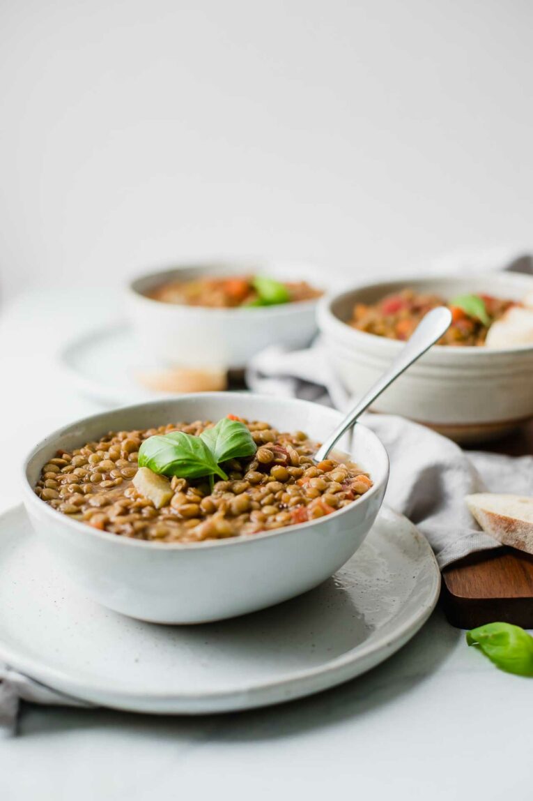 Angled shot of vegan lentil soup in a grey bowl on top of a grey plate.