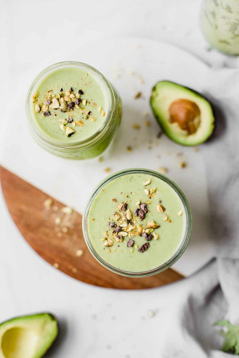 Top shot of green avocado smoothie in mason jars on a cutting board.