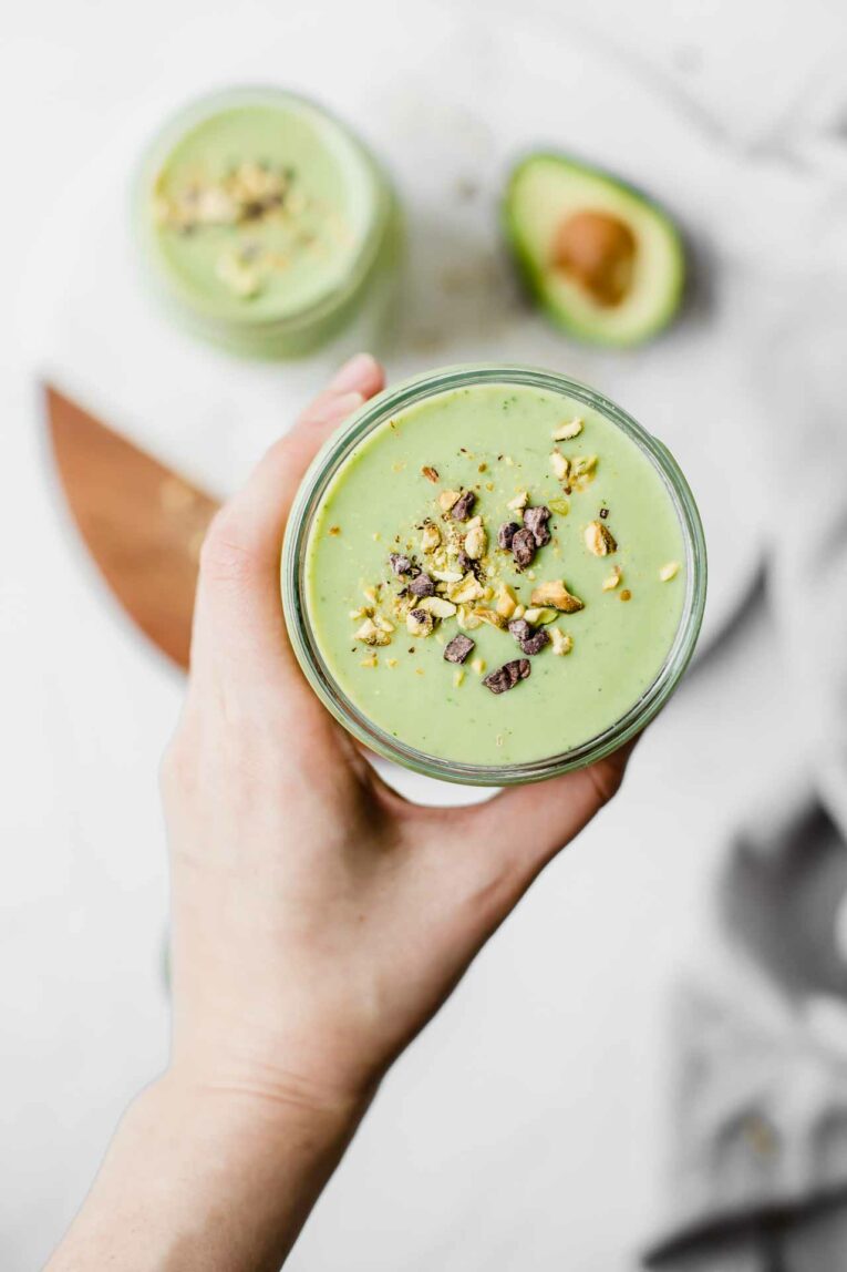 Top shot of hand holding green avocado smoothie.