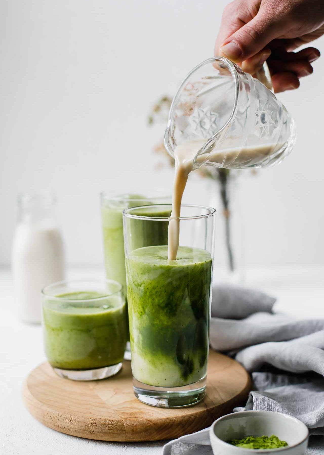A hand pouring milk into a matcha latte.