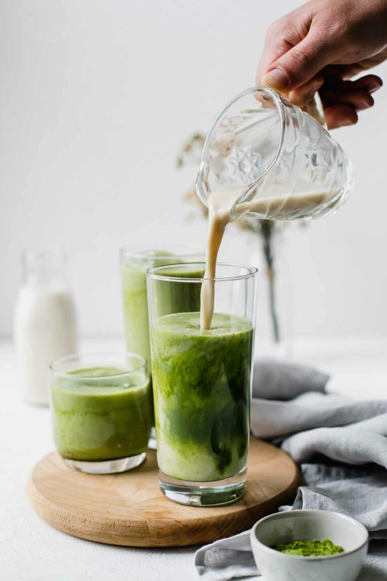 A hand pouring milk into a matcha latte.