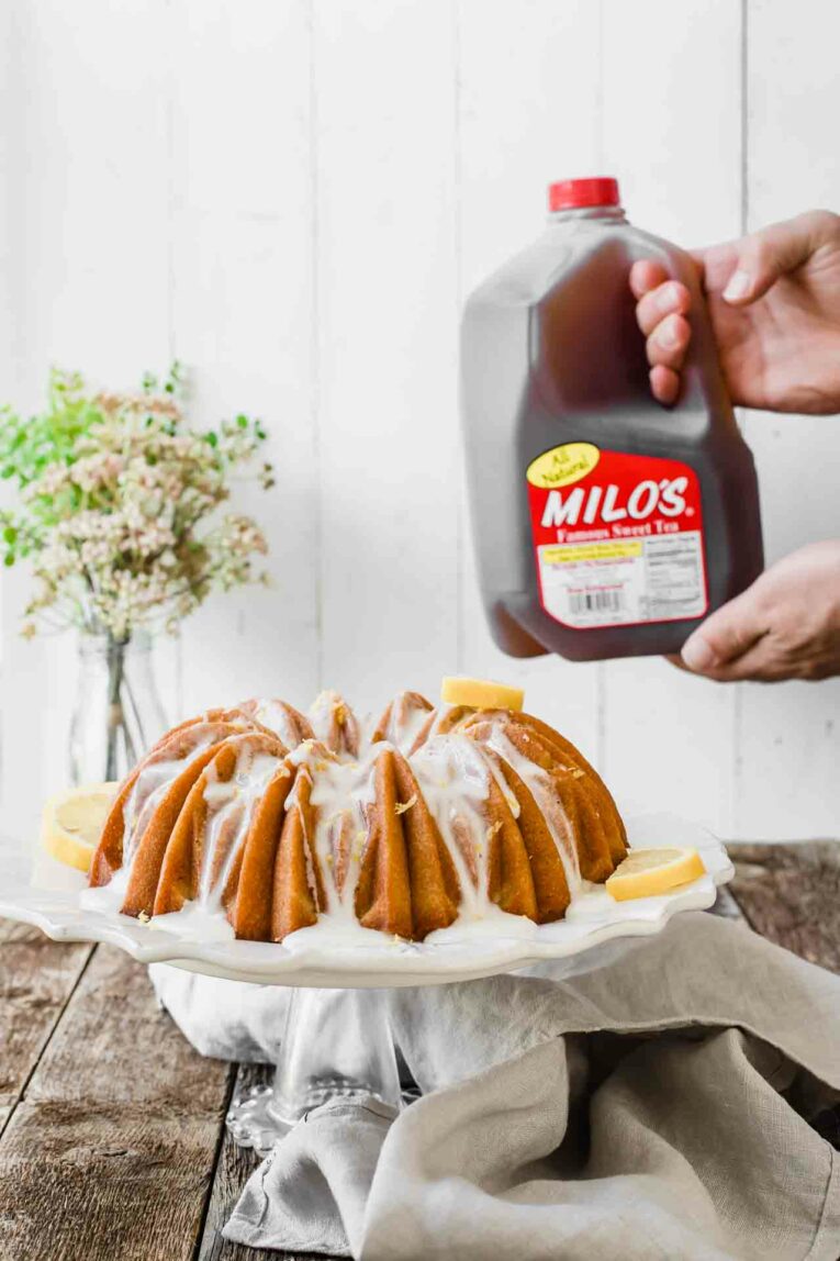 Looking for an easy dessert that will impress your guests at your next summer gathering? This Southern Sweet Tea Lemon Cake is light, fluffy, sweet, and tastes like everything summer! Easy southern sweet tea lemon cake on a cake stand. made with Milo's famous sweet tea!