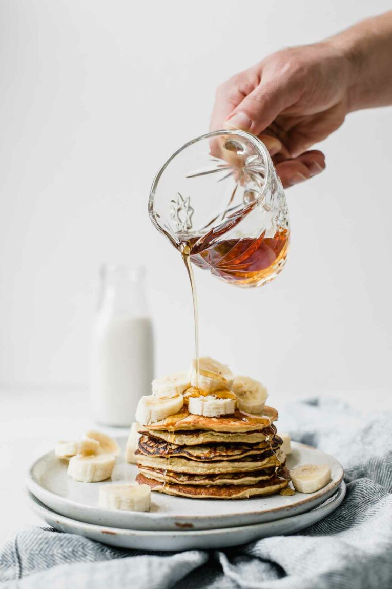 The BEST ever Healthy Banana Pancakes that can be made in 10 minutes or less! Made with real banana, protein-loaded eggs, rolled oats, and plant-based protein powder. So delicious and perfect for your entire family! Syrup poured over healthy banana pancakes.