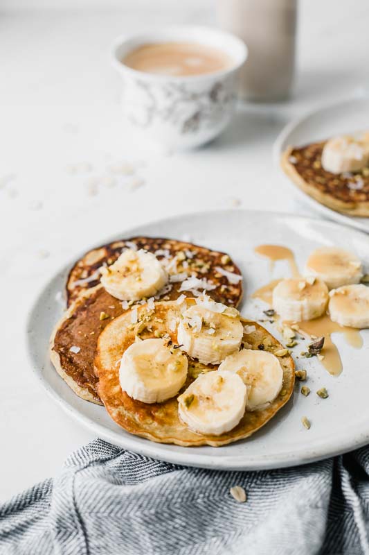 Healthy Banana Pancakes topped with bananas, pistachios, coconut, and served with a latte.