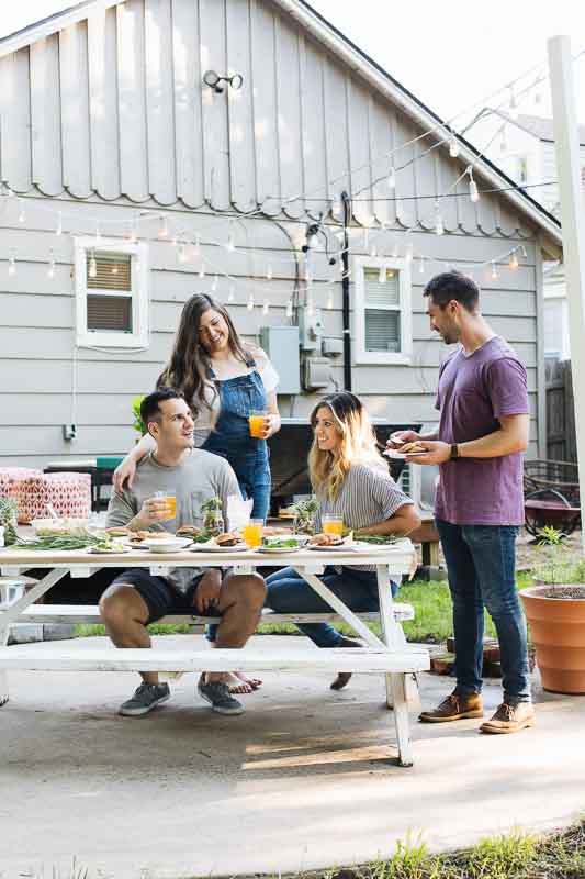 Friends hanging out and eating at a casual summer gathering in the backyard.